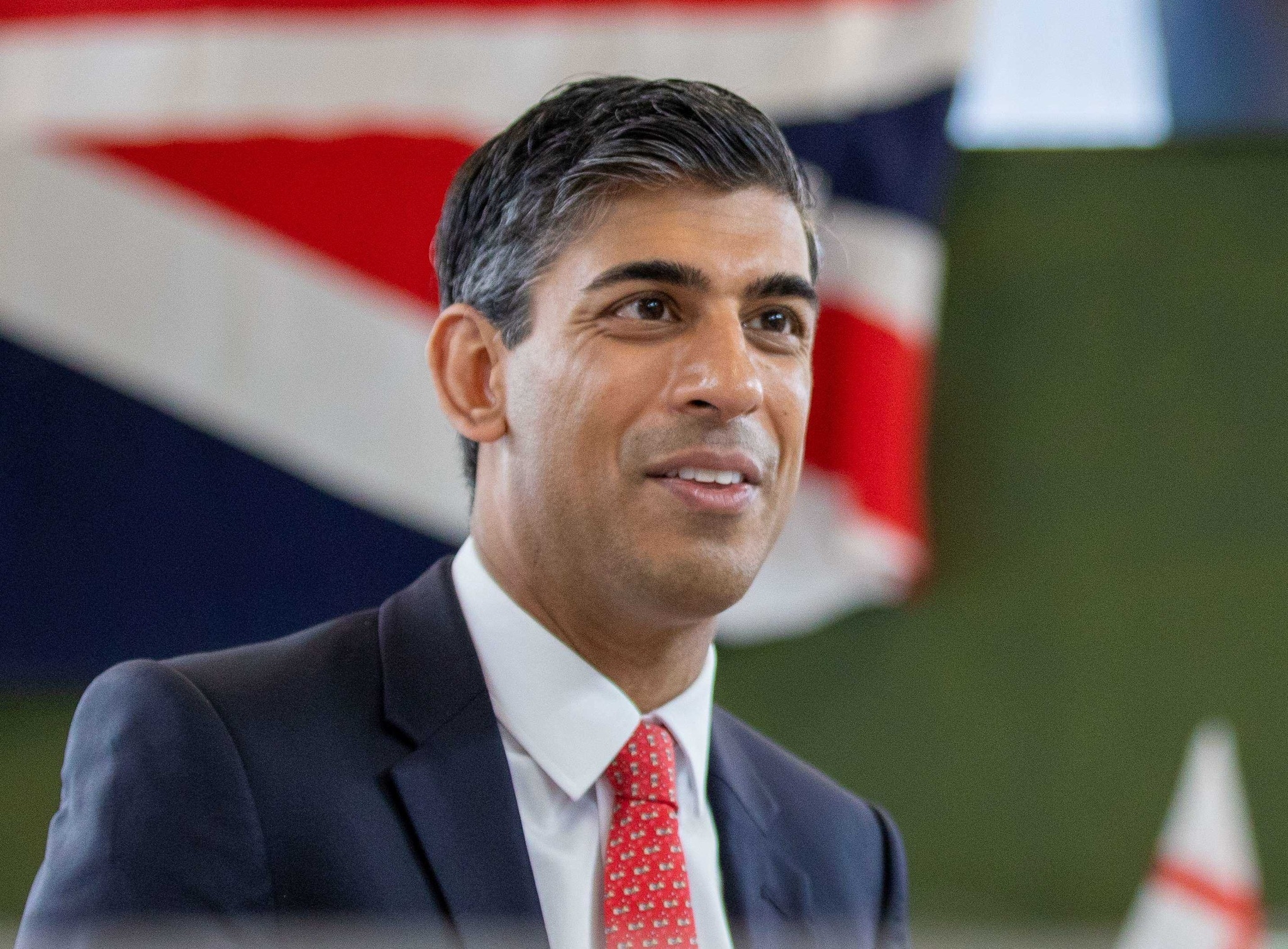 Rishi Sunak speaking in front of a raised union jack